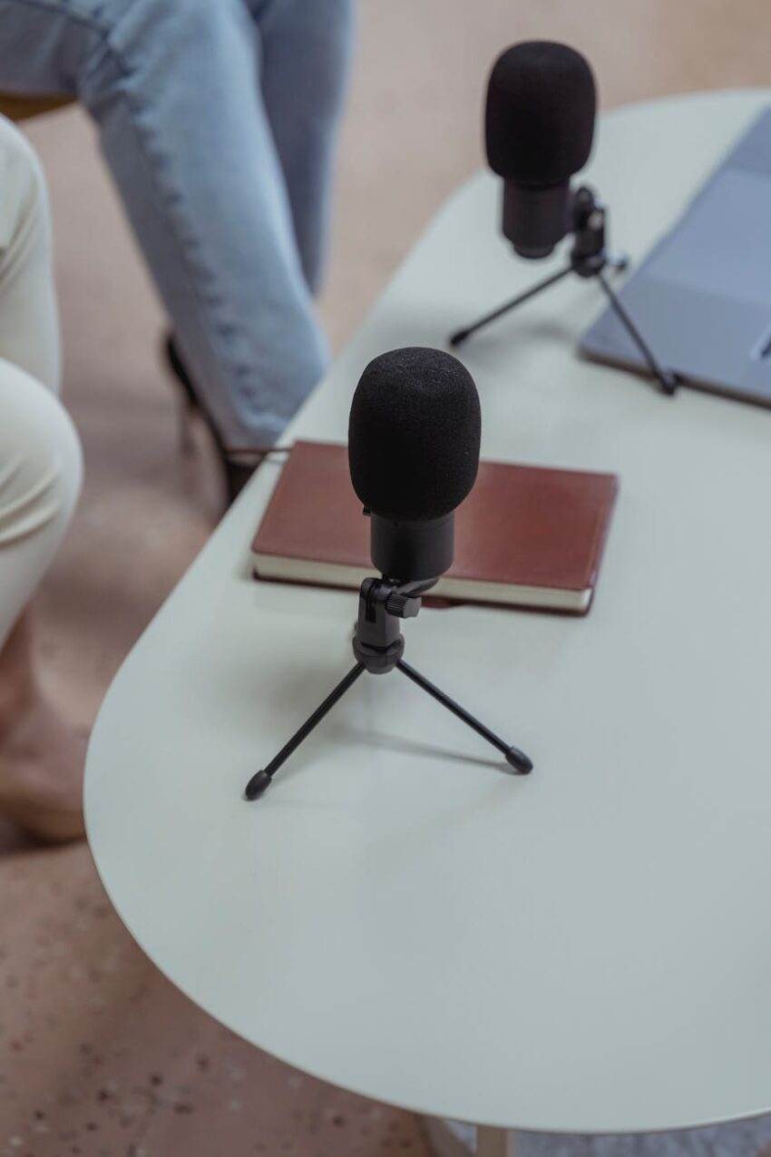 Close-up of microphones, a notebook, and laptops on a white table, ideal for podcasting.