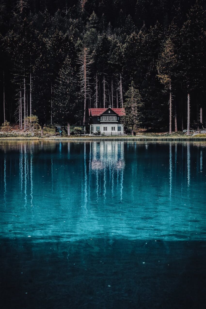 A picturesque house by a serene lake surrounded by lush forest reflecting in the clear blue water.