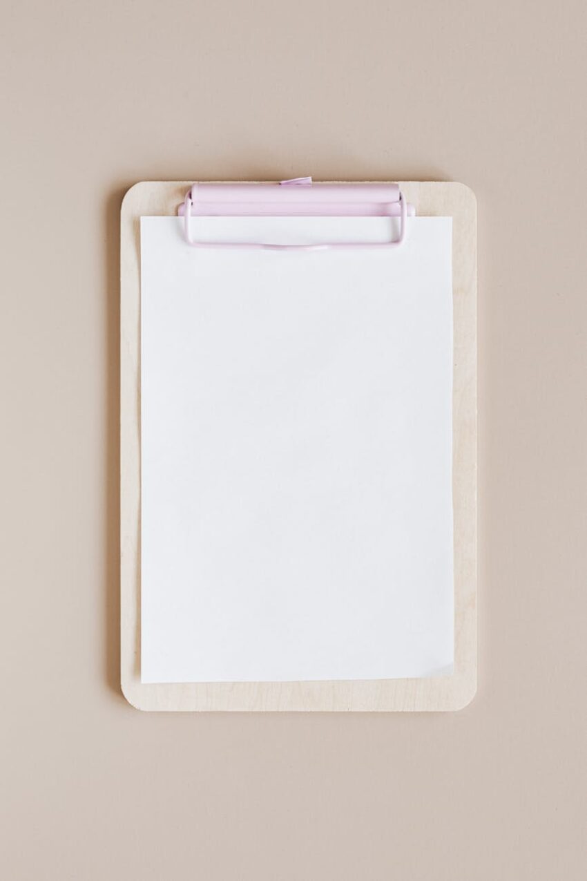 Top view of a minimalist wooden clipboard with blank paper against a neutral background.