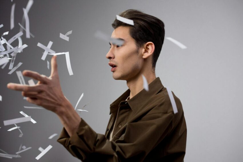 Engaging portrait captures a man with creative expression surrounded by flying papers on a gray background.