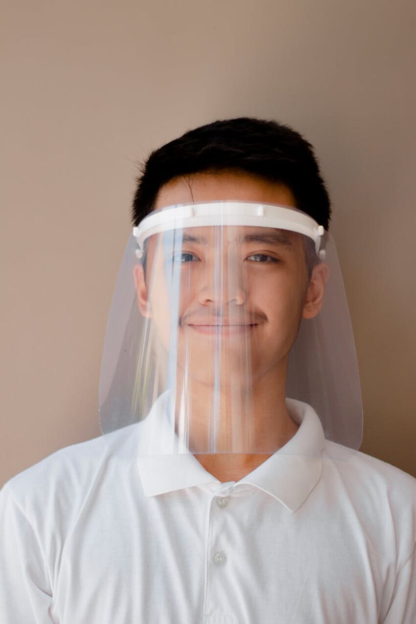Portrait of a smiling man wearing a clear face shield for protection.