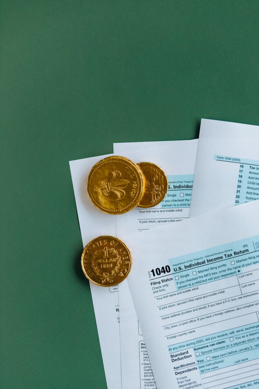 U.S. tax forms accompanied by gold coins, on a green surface, symbolizing finance.