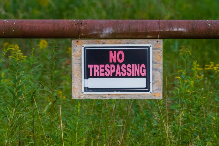 No trespassing sign on a rusty fence in a grassy field