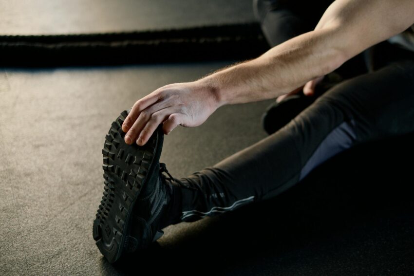 Close-up of a man's hand reaching for his foot while stretching on a gym floor.