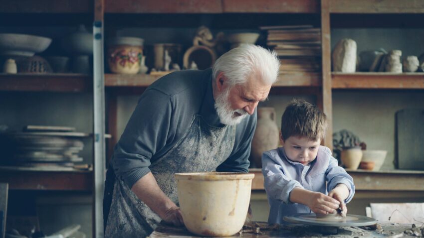 Elderly man guides young boy in pottery making, conveying skill and creativity.