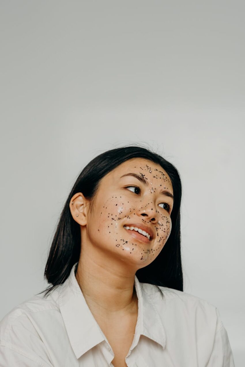 Asian woman smiling with a glitter face mask in a wellness and beauty studio setting.