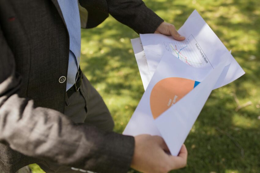 Man in suit holding financial reports in a sunny park.