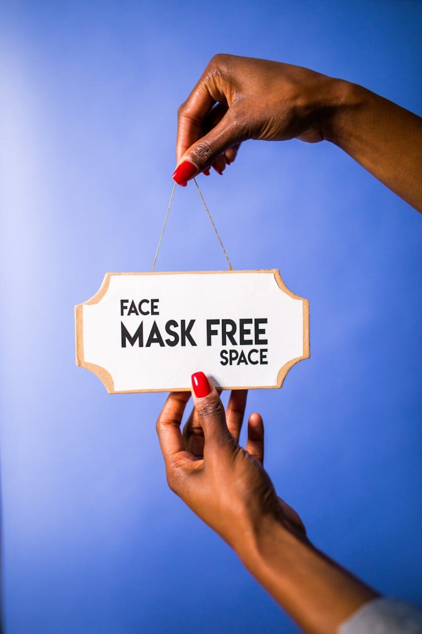 Close-up of hands holding a sign with 'Face Mask Free Space' text, against a blue background.
