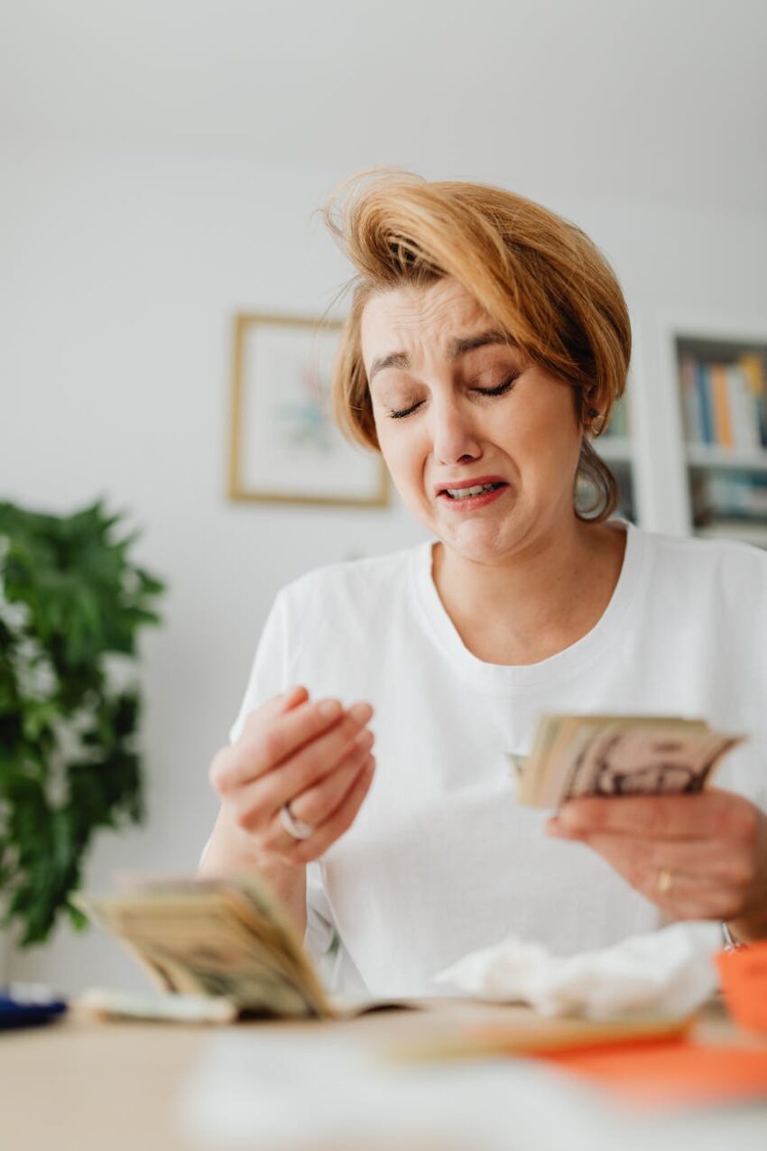Upset woman counting money, expressing financial stress indoors.