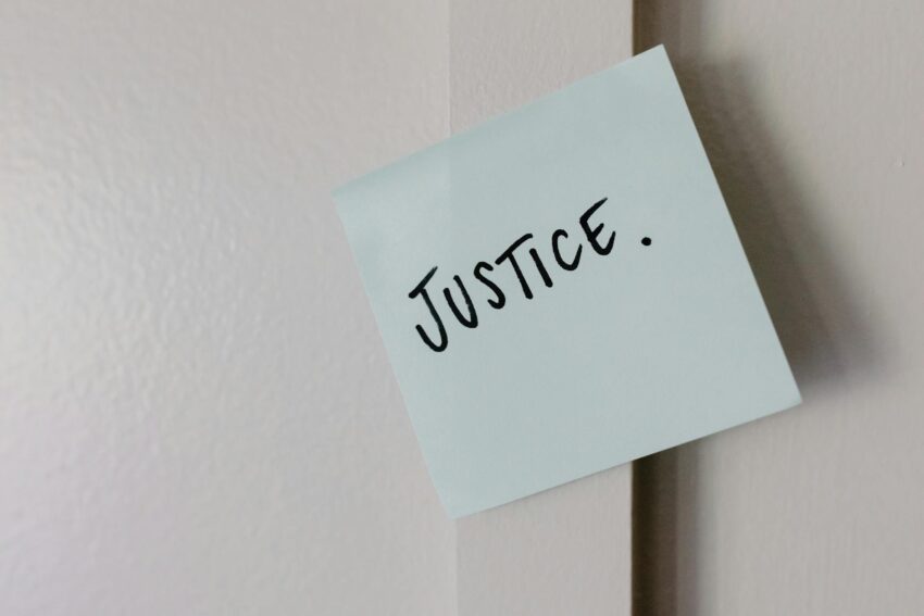 A sticky note with handwritten 'Justice' message on a white wall.