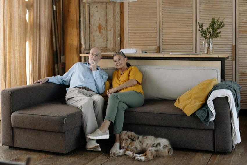 Charming scene of an elderly couple enjoying a cozy moment with their dog on a sofa in a rustic home.
