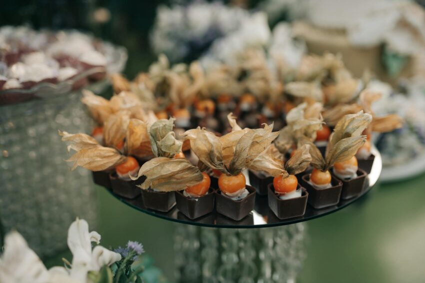 Delicate chocolate desserts topped with physalis on a mirrored tray, perfect for special events.
