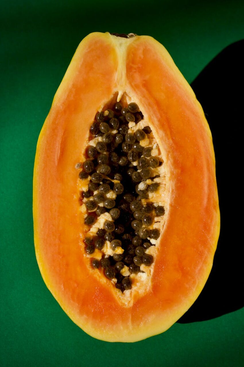 Close-up of half a papaya showcasing seeds against a green backdrop.