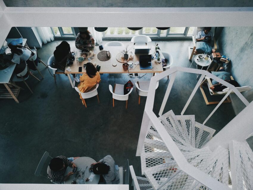 Overhead view of a modern workspace with people around tables and a spiral staircase.