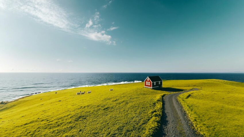 Breathtaking view of a red house on a green hill by the sea, featuring countryside tranquility.