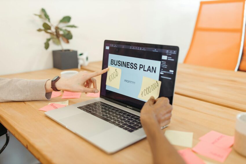 Hands collaborate on a business plan with a laptop in a modern office setting.