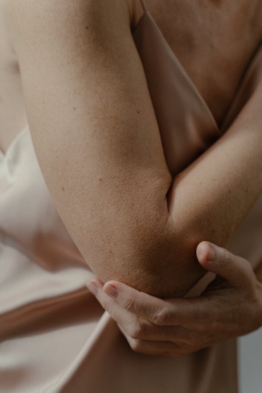 A soft focus close-up of a person's arm touching the elbow in gentle light.