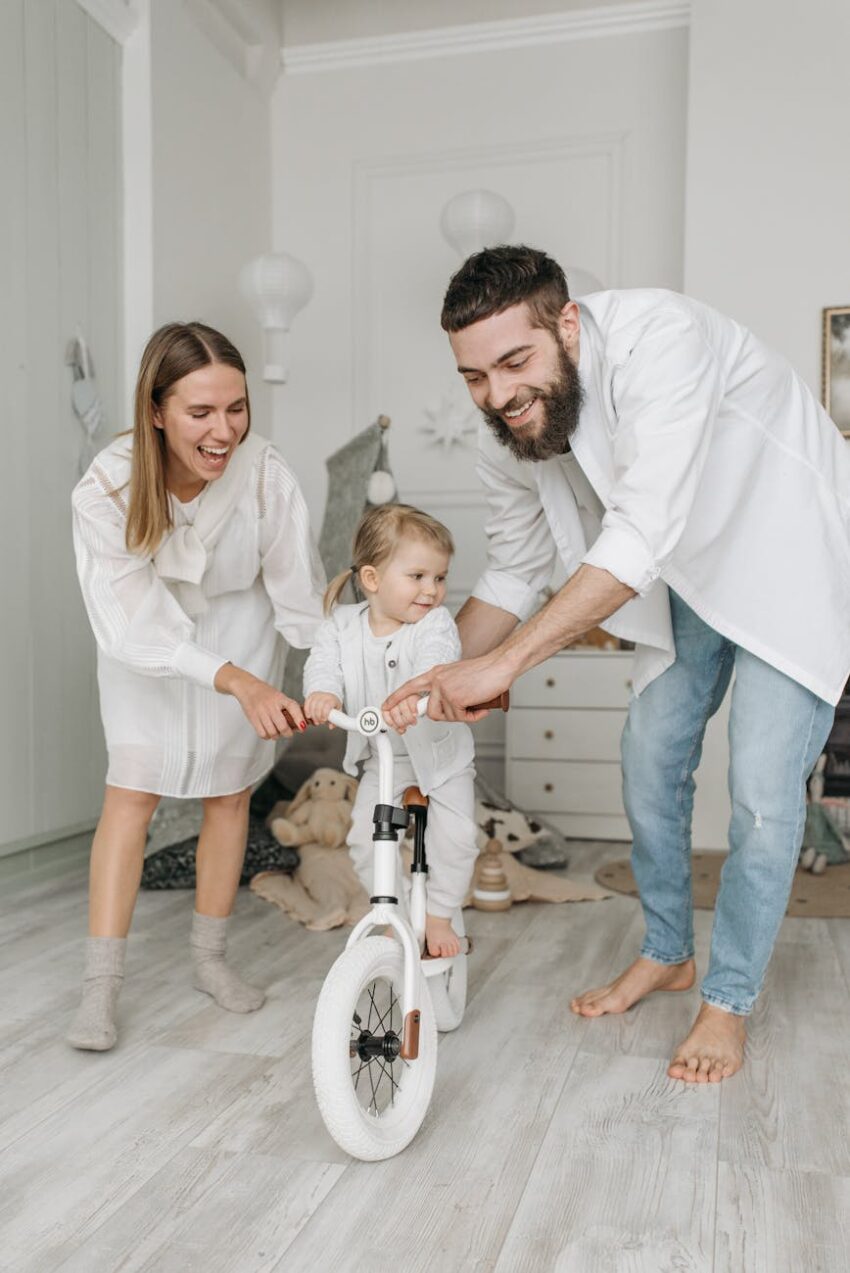 Joyful family bonding indoors as parents assist child on bicycle. Bright and cheerful moment.