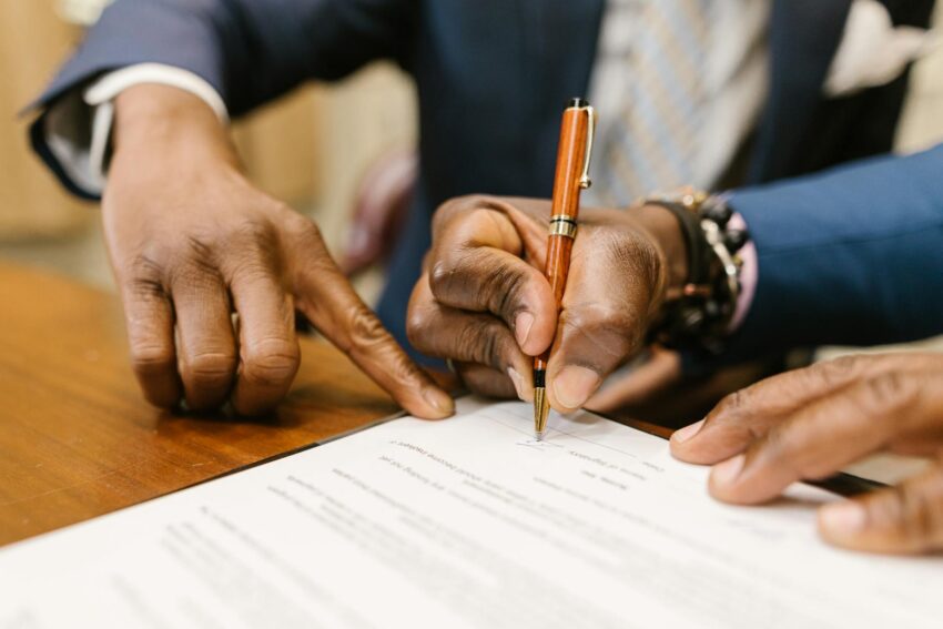 Close-up of business professionals signing a legal contract in an office setting.