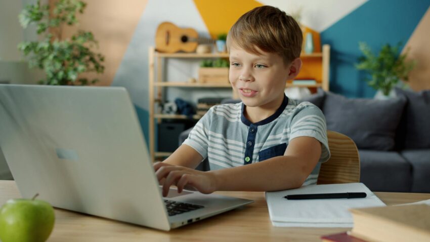 Young boy using a laptop for online learning at home with study materials nearby.