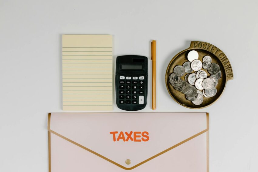 A flat lay of tax preparation essentials: calculator, coins, notepad, pen, and folder.
