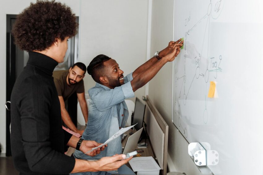A diverse team of professionals brainstorming solutions at a whiteboard in an office setting.