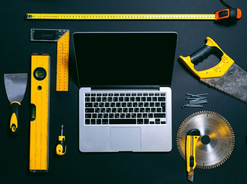 Overhead view of a laptop surrounded by various hand tools on a dark background, representing technology and construction.