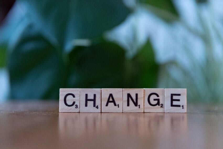 Scrabble tiles spelling 'CHANGE' on a wooden surface with a blurred green background.